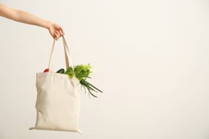 Main tenant un sac en coton rempli de légumes frais contre un mur blanc
