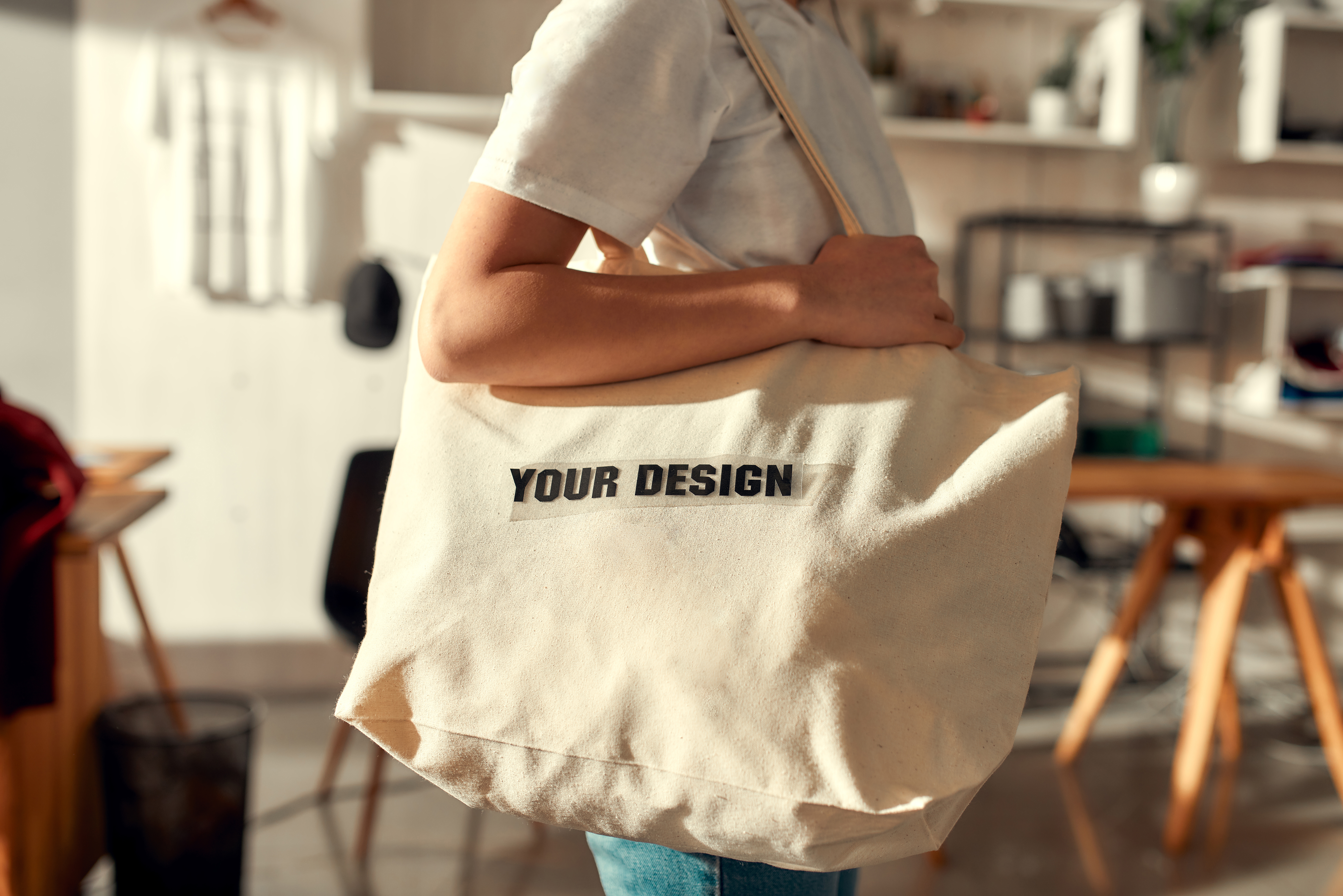 Personne portant un sac fourre-tout beige prêt à être personnalisé, dans un environnement lumineux et moderne